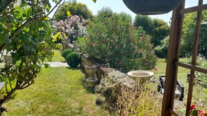 Un jardin avec un chemin de pierres, une pergola en bois et diverses plantes et fleurs.