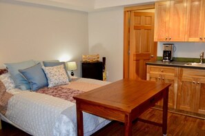 Een slaapkamer met een bed, kussens, een nachtkastje en een bijzettafeltje. Er staat een houten tafel in het midden van de kamer.