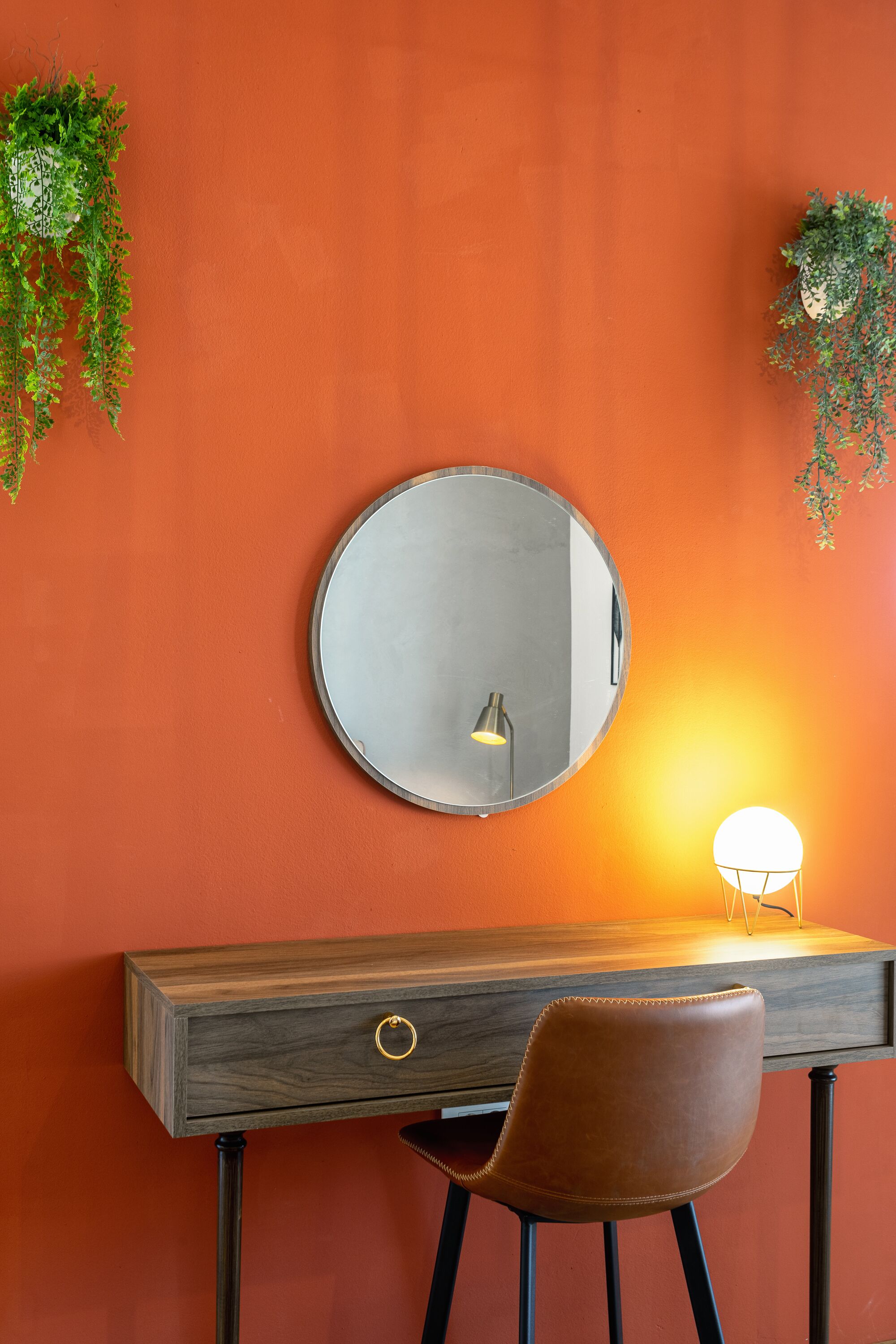 A desk with a round mirror, a chair, and a small lamp.