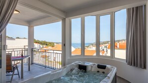 Ein Wellnessbereich mit Whirlpool und einem Balkon mit Blick auf das Meer und Gebäude.