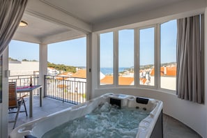A spa area with a hot tub and a balcony with a view of the sea and buildings.