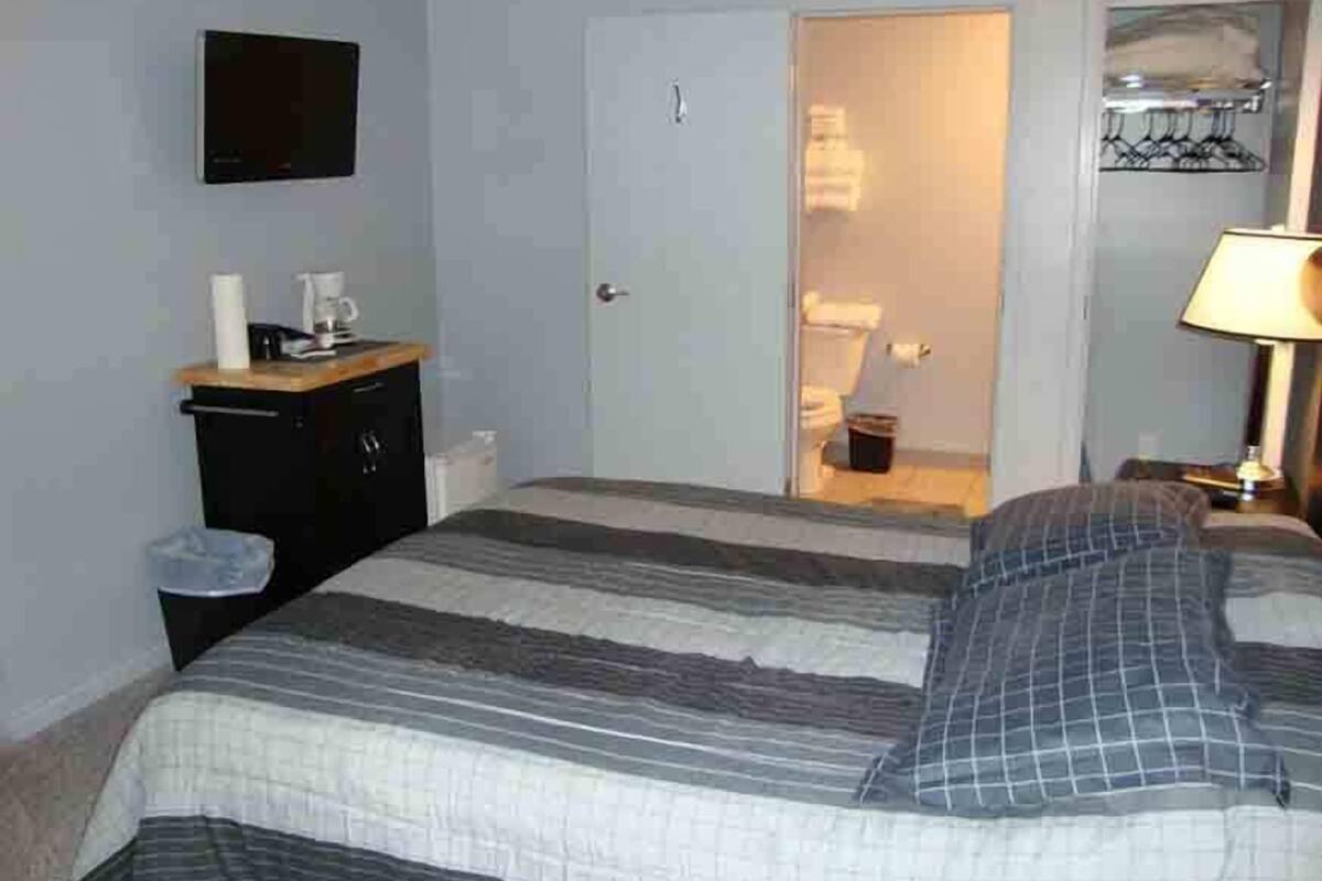 A bedroom with a bed, a desk with a lamp, a TV, and a door leading to a bathroom.