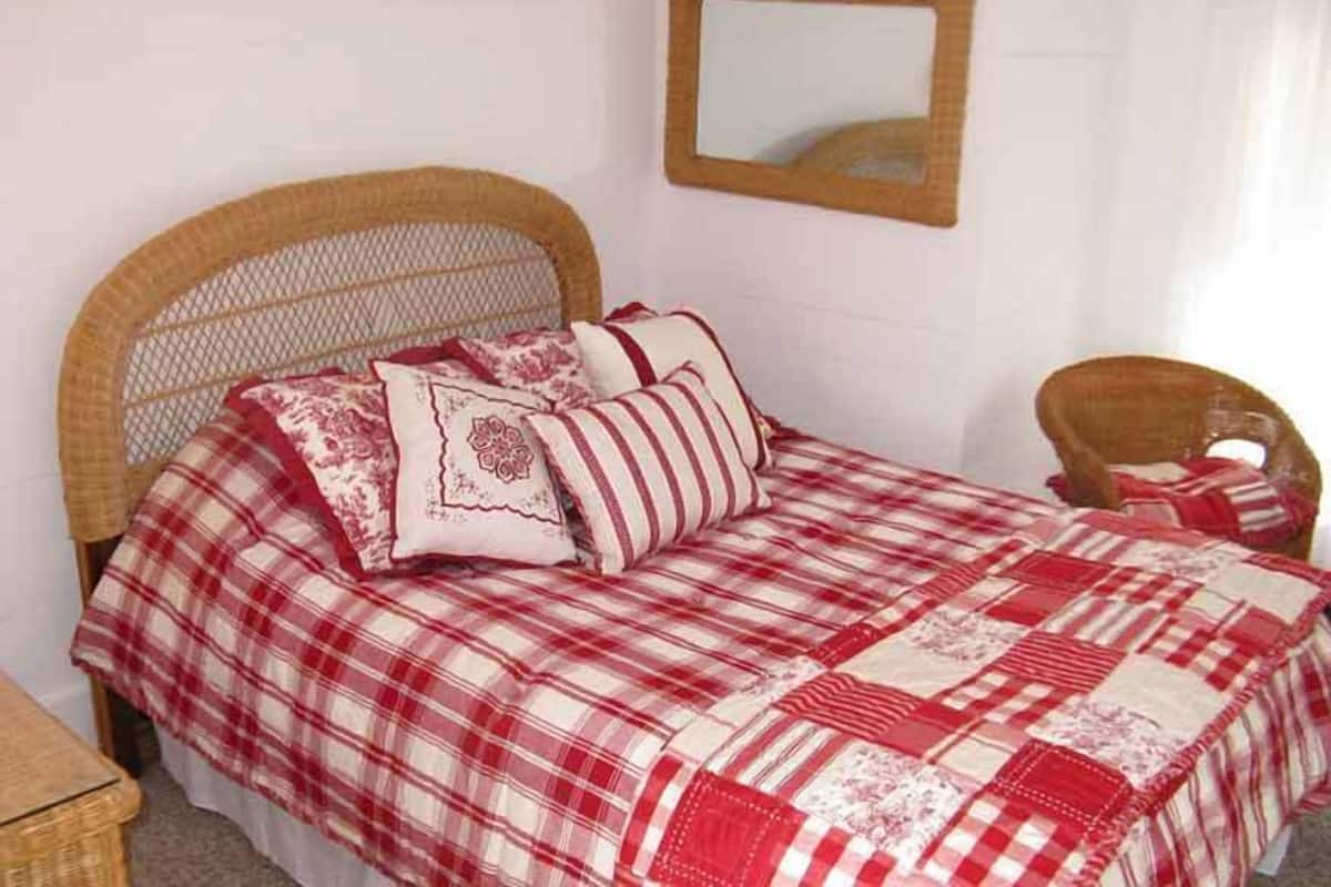 A bed with a checkered bedspread, a wicker headboard, and several pillows.