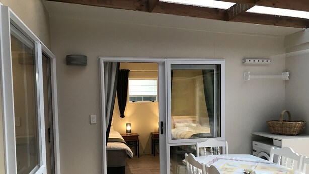 A cozy room with a bed, a table, and a chair. There is a sliding door leading to another room. - Angie's Rural Retreat (Lower Hutt)