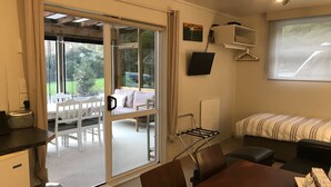 A room with a sliding glass door leading to an outdoor seating area, a bed with a striped blanket, a TV mounted on the wall, and a table with a tray of items. - Angie's Rural Retreat (Lower Hutt)