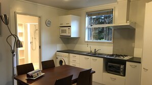 A compact kitchen with a microwave, oven, sink, and a dining area with a table and chairs. - Angie's Rural Retreat (Lower Hutt)