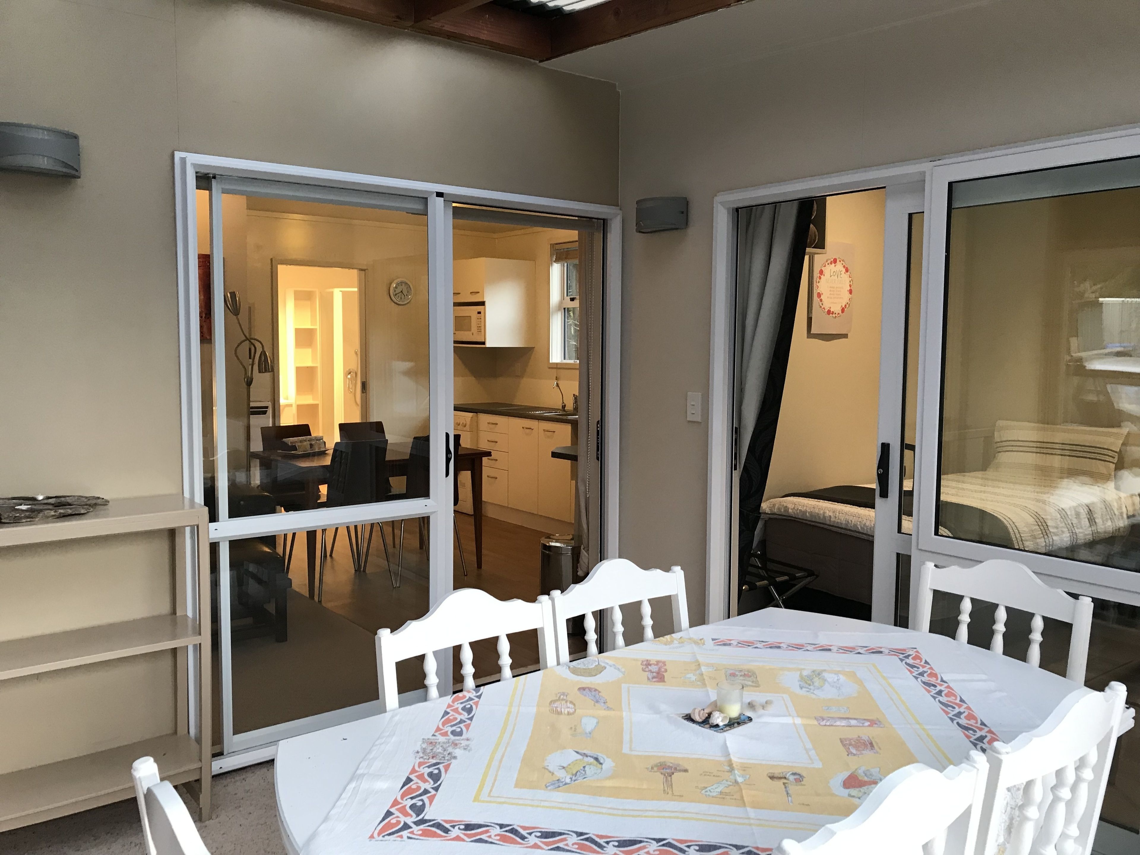 Un comedor con una mesa dispuesta para dos, una silla blanca y un puerta de vidrio que da a una cocina.