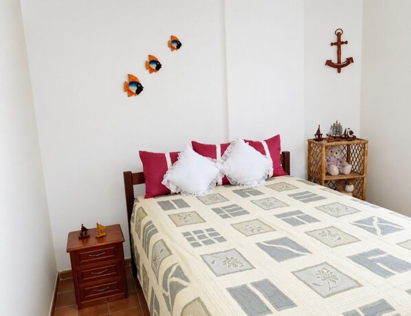A bedroom with a bed, pillows, a nightstand, a dresser, and wall decorations including fish and an anchor.