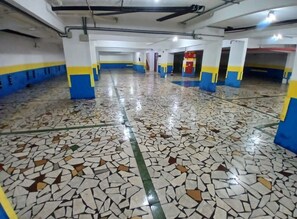 Un vaste espace intérieur doté d’un sol carrelé, de piliers ornés de rayures bleues et jaunes, et d’un plafond laissant apparaître des tuyaux et des luminaires.