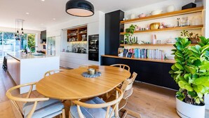 Una cocina moderna con una isla central, mesa de comedor de madera y estanterías empotradas con libros y objetos decorativos.
