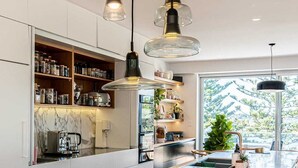 Una cocina moderna con una isla grande, lámparas colgantes y vistas al exterior con vegetación.
