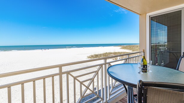 Un balcon donnant sur une plage, une table avec une bouteille et des verres, et une chaise.