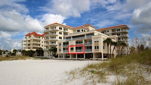 Un hôtel en bord de mer doté de nombreux balcons, une plage de sable en premier plan et un ciel dégagé.