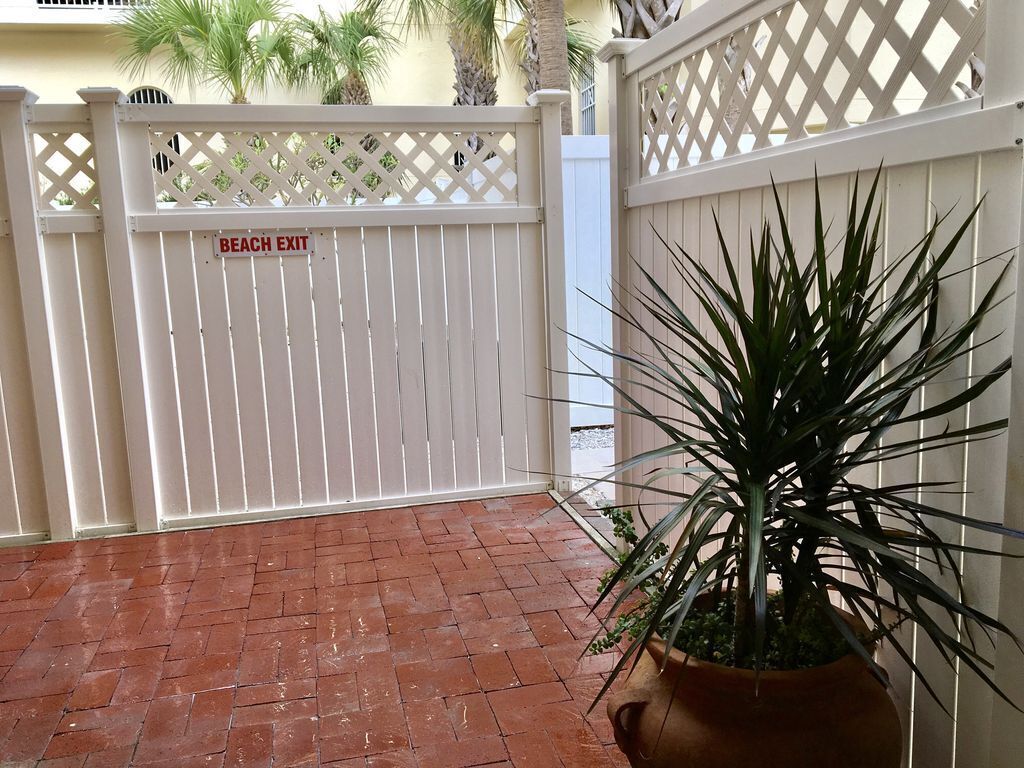 A gated area with a 'BEACH EXIT' sign, a potted plant, and a brick patio.