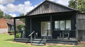 A rustic wooden building with a porch, a small table, and two chairs. - Loyd Hall Plantation (Cheneyville)