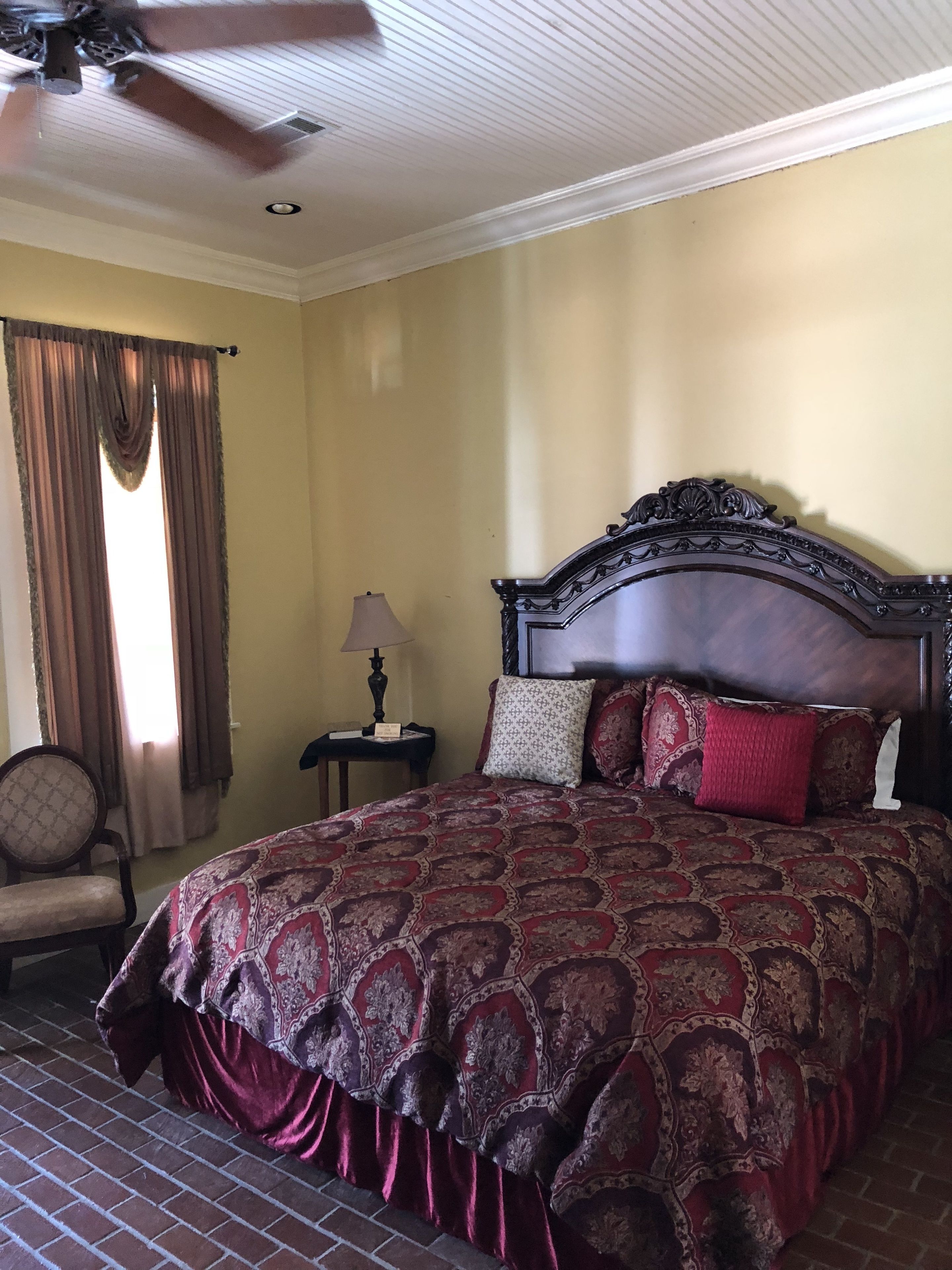 A hotel room with a large bed, a ceiling fan, a nightstand with a lamp, and a chair.