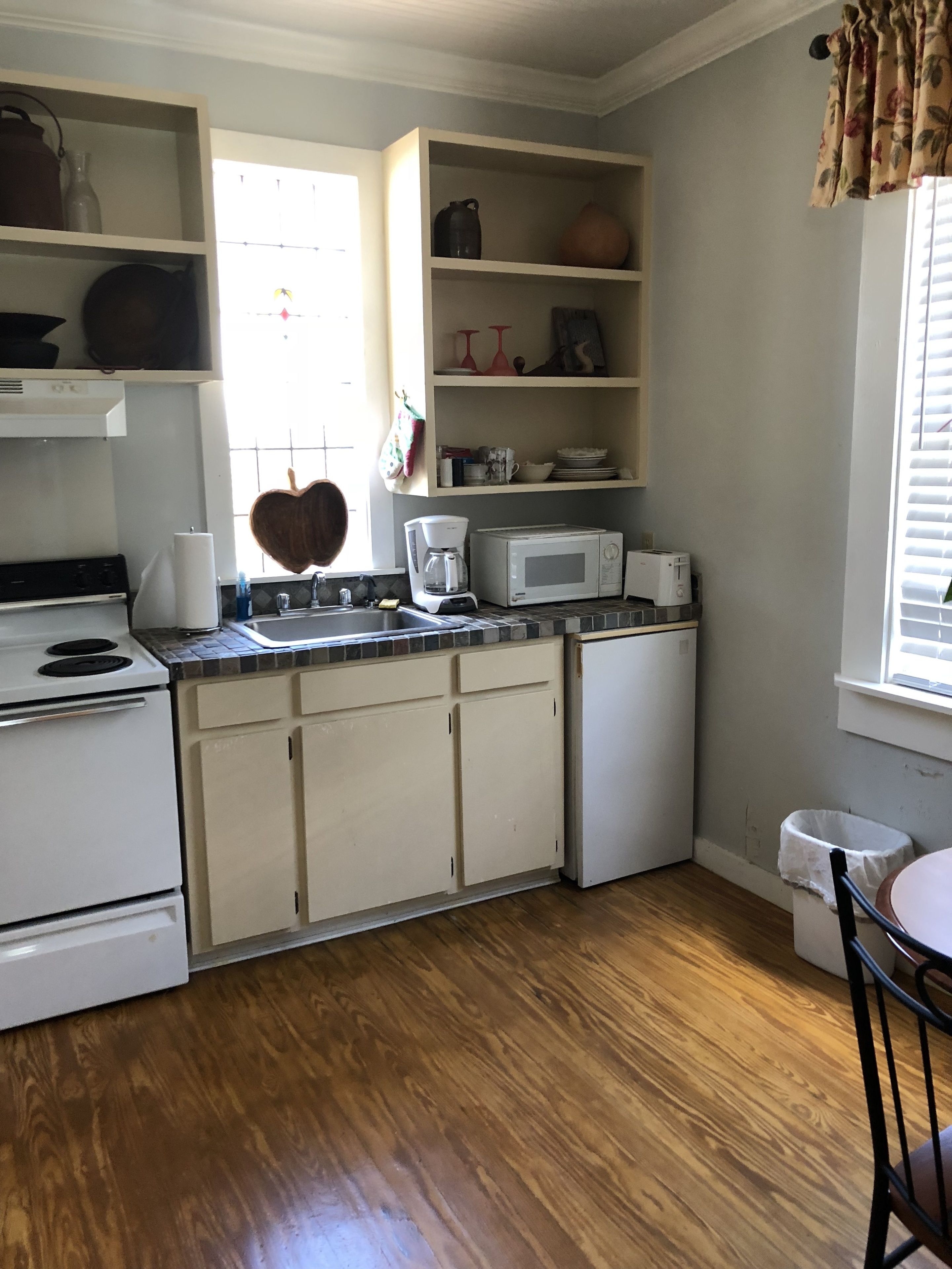 A compact kitchen with white cabinets, a microwave, a coffee maker, and a sink.