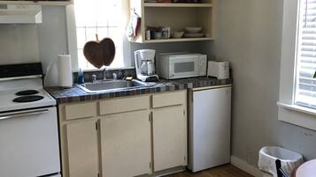 A compact kitchen with white cabinets, a microwave, a coffee maker, and a sink.