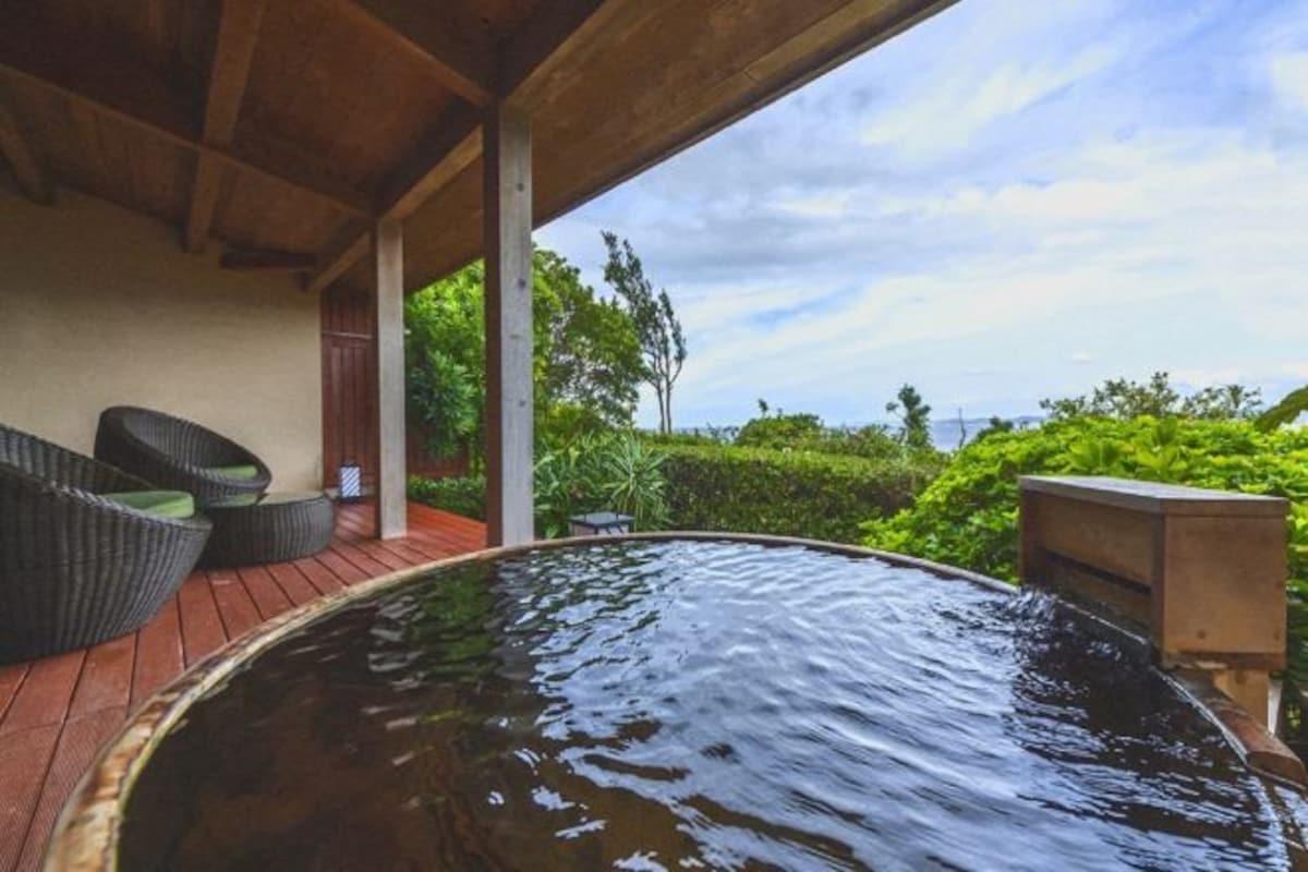 Un área de hidromasaje con terraza de madera, mobiliario de mimbre y vistas a la vegetación.