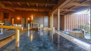 A traditional Japanese onsen with stone flooring, wooden beams, and a wooden fence in the background.