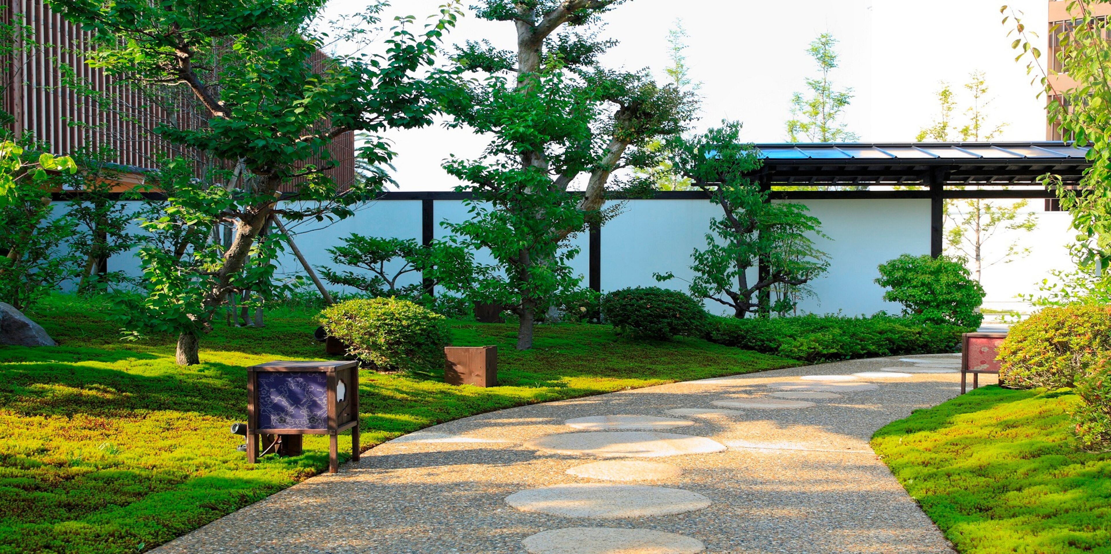 A pathway with stepping stones leading to a building with a modern design, surrounded by lush greenery and trees.