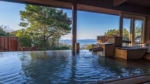 Baño de aguas termales con bancos de madera y vista al mar.