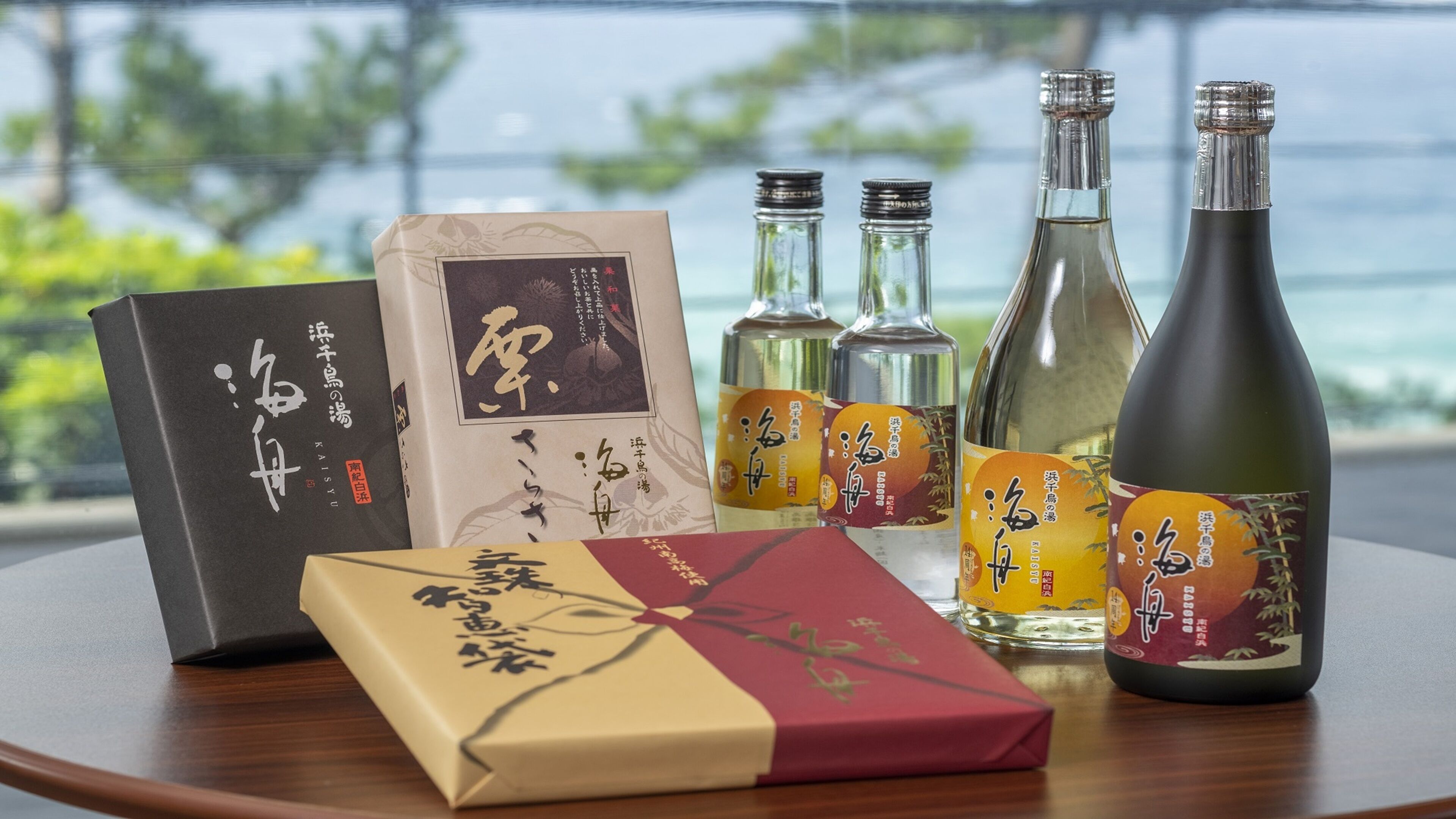 A table with various items including books, bottles, and boxes, with a view of greenery and water in the background.