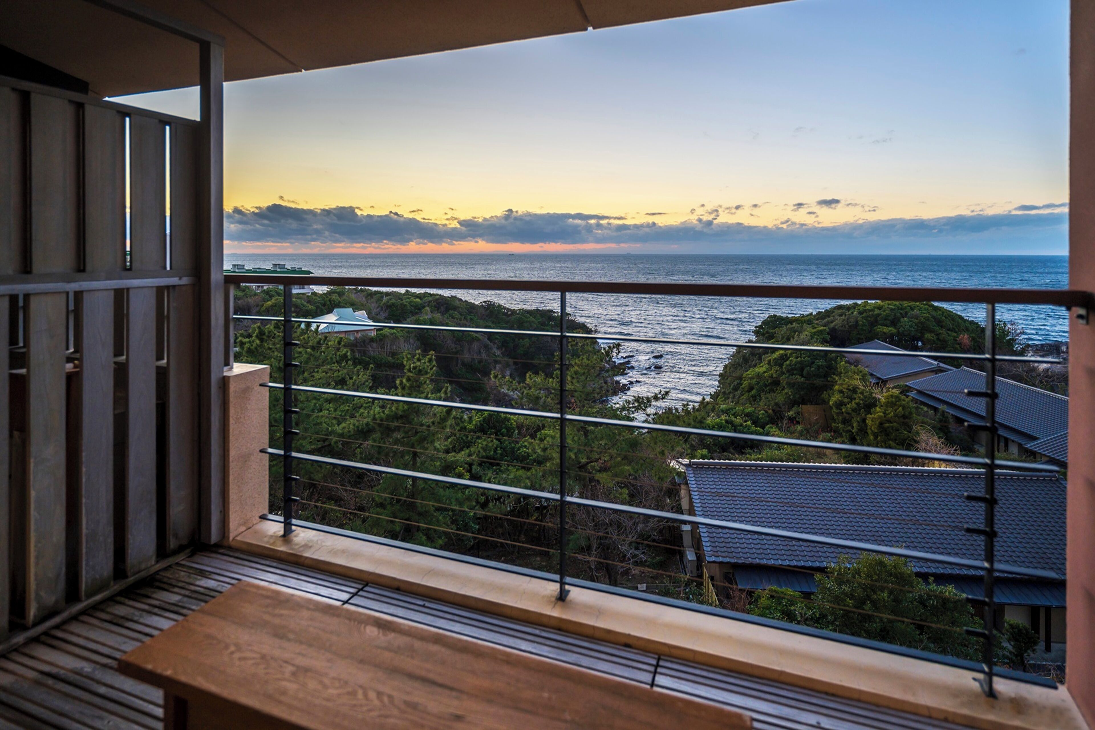 A balcony with a view of the sea and surrounding greenery.