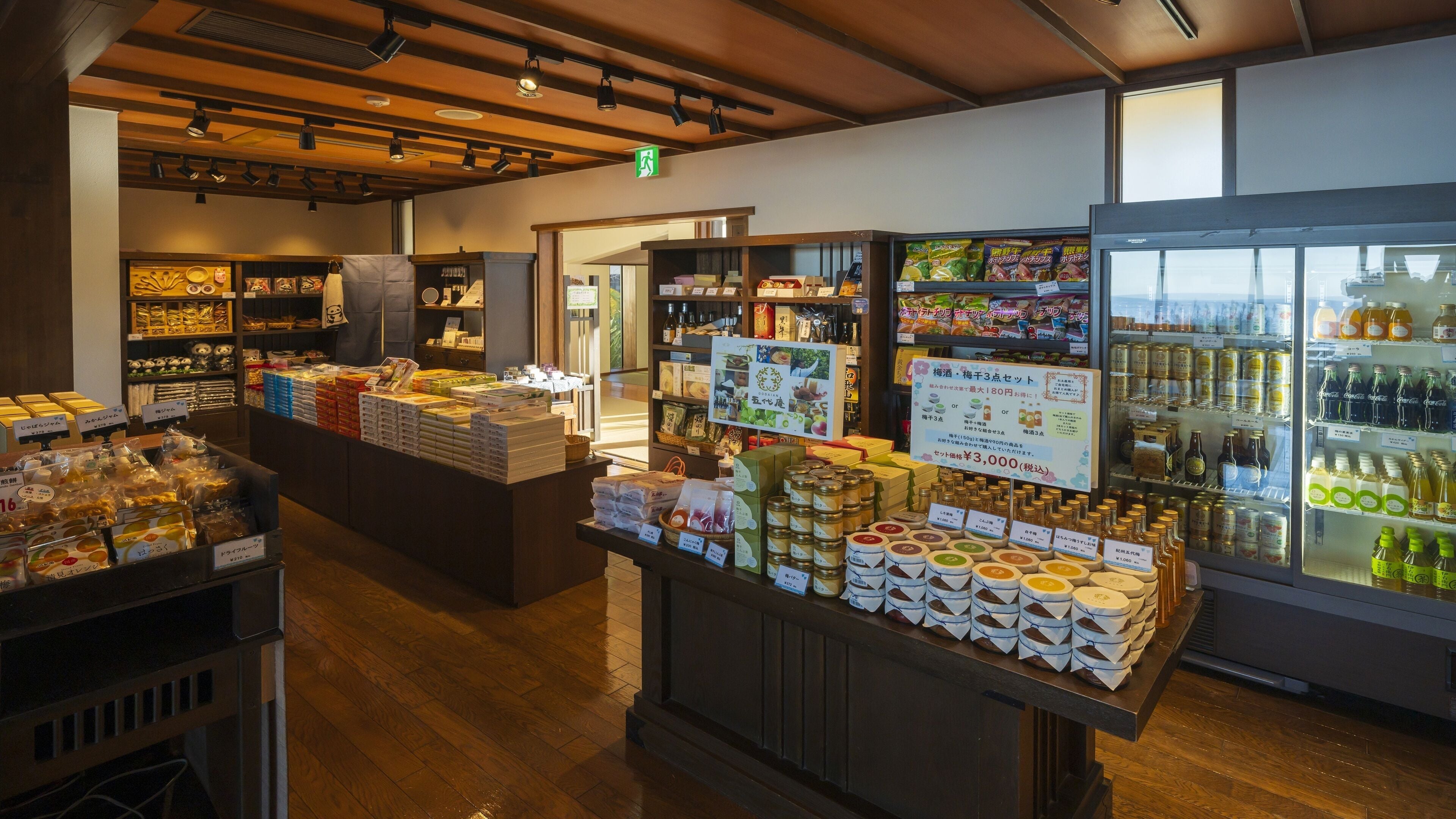 Een winkelinterieur met schappen vol diverse producten, een koelvitrine en een houten toonbank met verpakte goederen.