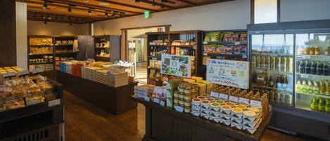 Interior de una tienda con estantes llenos de diversos productos, un expositor refrigerado y un mostrador de madera con productos envasados.
