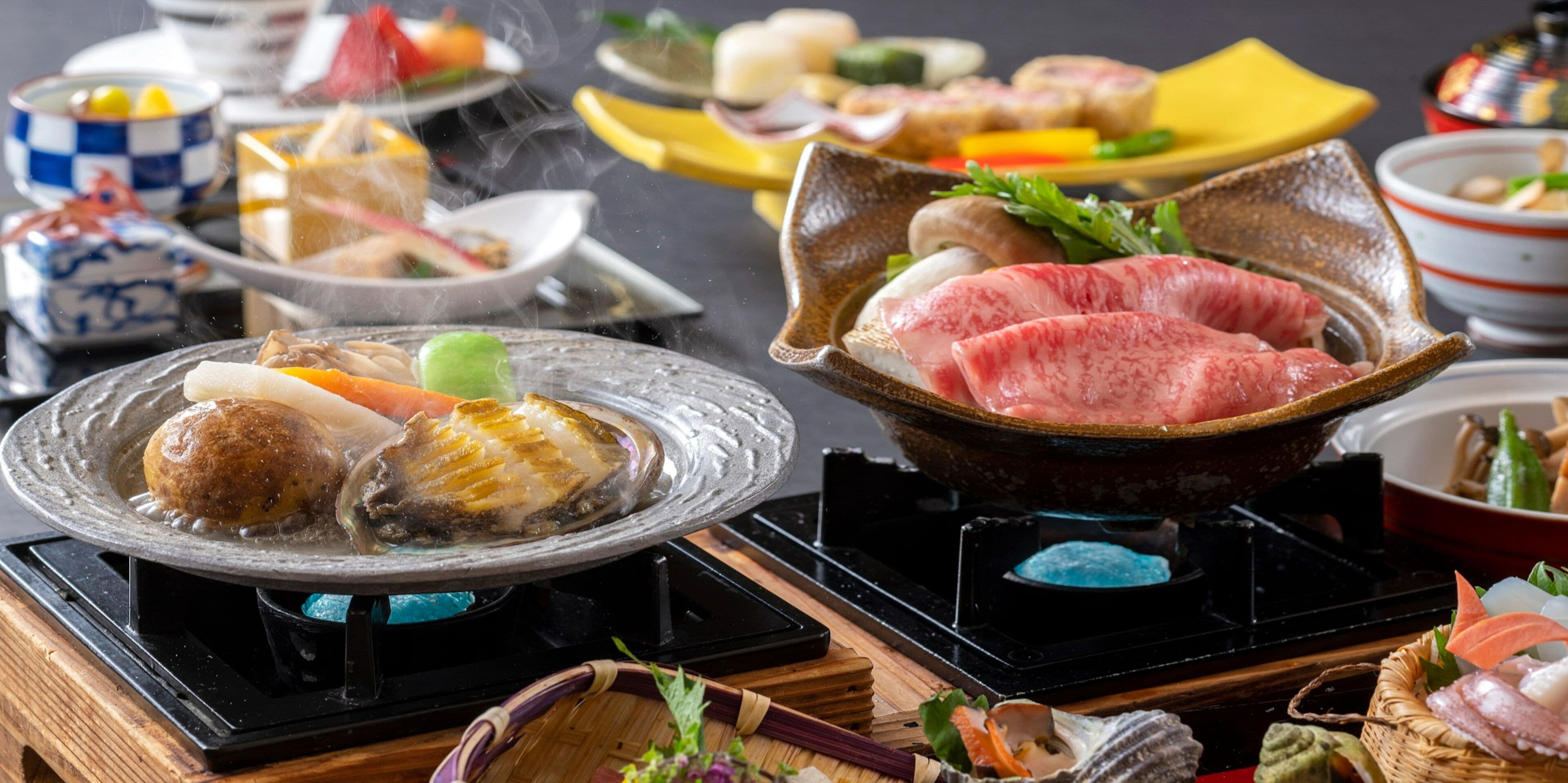 Variedad de platos en una mesa, incluyendo mariscos y carne, con una tetera y tazas al fondo.