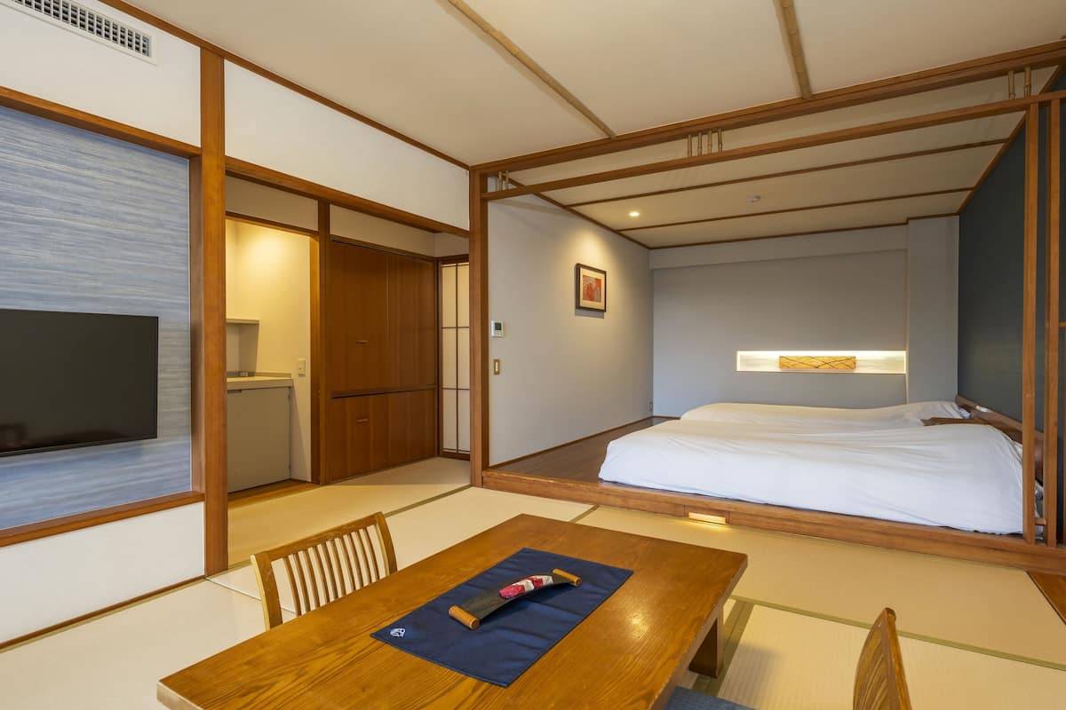 Een traditionele Japanse kamer met tatami vloeren, een houten bed, een televisie en een tafel met kussen.