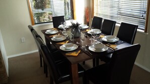 A dining table set for six with black chairs, white plates, and clear glasses.