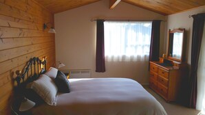 A bedroom with a wooden ceiling, a bed with pillows, a dresser, a mirror, and a window with curtains.