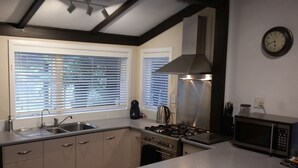 A modern kitchen with a gas stove, stainless steel appliances, a microwave, and a window with blinds.