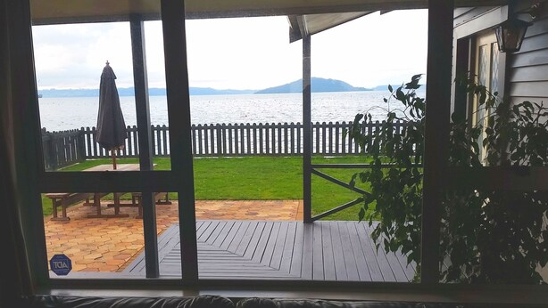 A view through a screened door to a deck with a wooden floor, a white picket fence, and a grassy area.