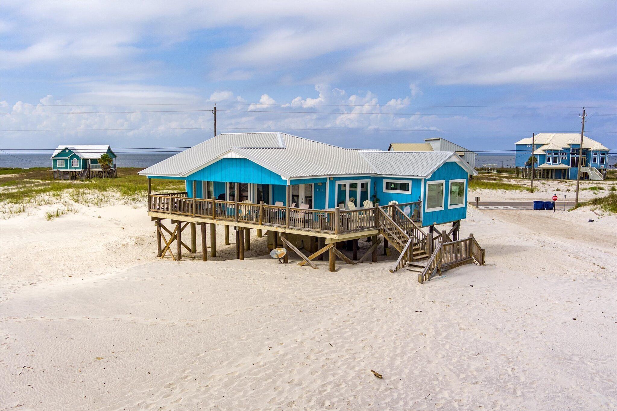 Une maison de plage bleue avec une terrasse en bois et un escalier menant à l’entrée.