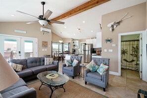 A spacious living area with a ceiling fan, a glass coffee table, and a grey sofa set.