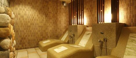 A spa room with two massage chairs, a stone wall, and a tiled floor.