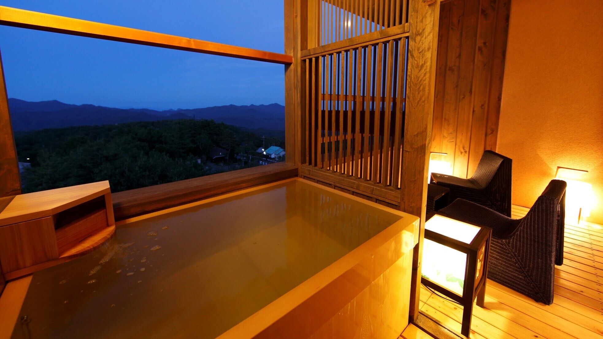 A hot tub with wooden railings and chairs, a view of mountains, and a wooden deck.