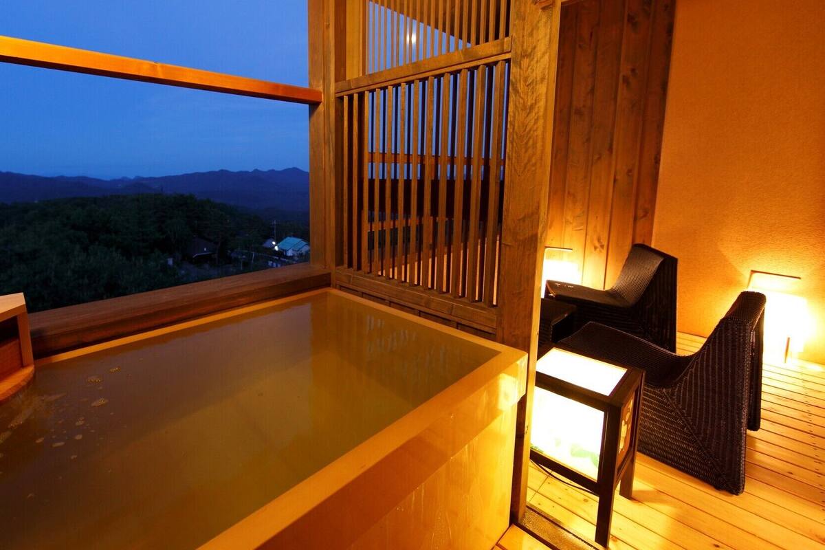 Un bain à remous avec des rampes et des chaises en bois, une vue sur les montagnes et une terrasse en bois.