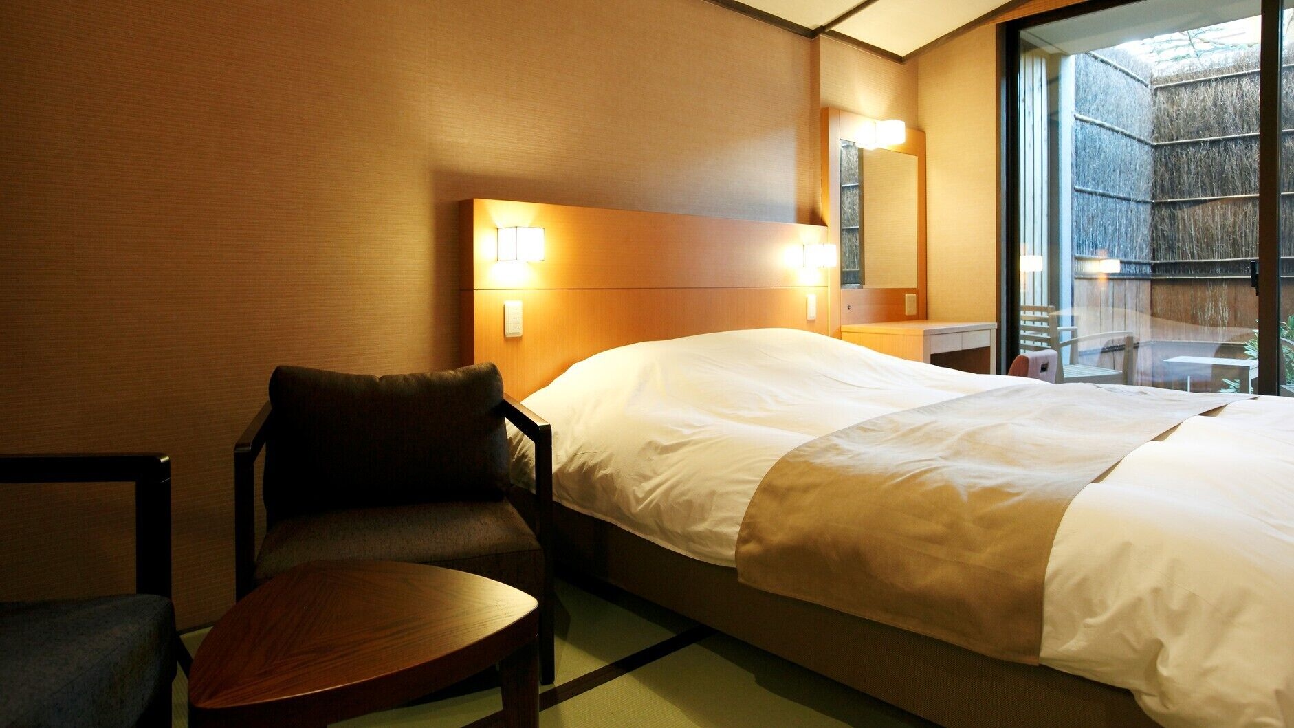 Une chambre d’hôtel avec un lit, une chaise, une petite table et une fenêtre donnant sur un paysage agréable.