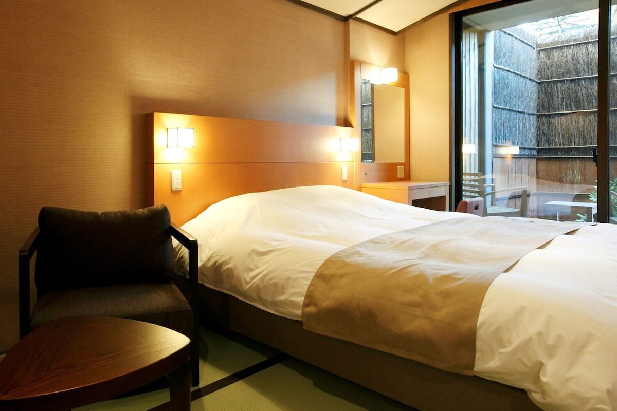 Une chambre d’hôtel avec un lit, une chaise, une petite table et une fenêtre donnant sur un paysage agréable.