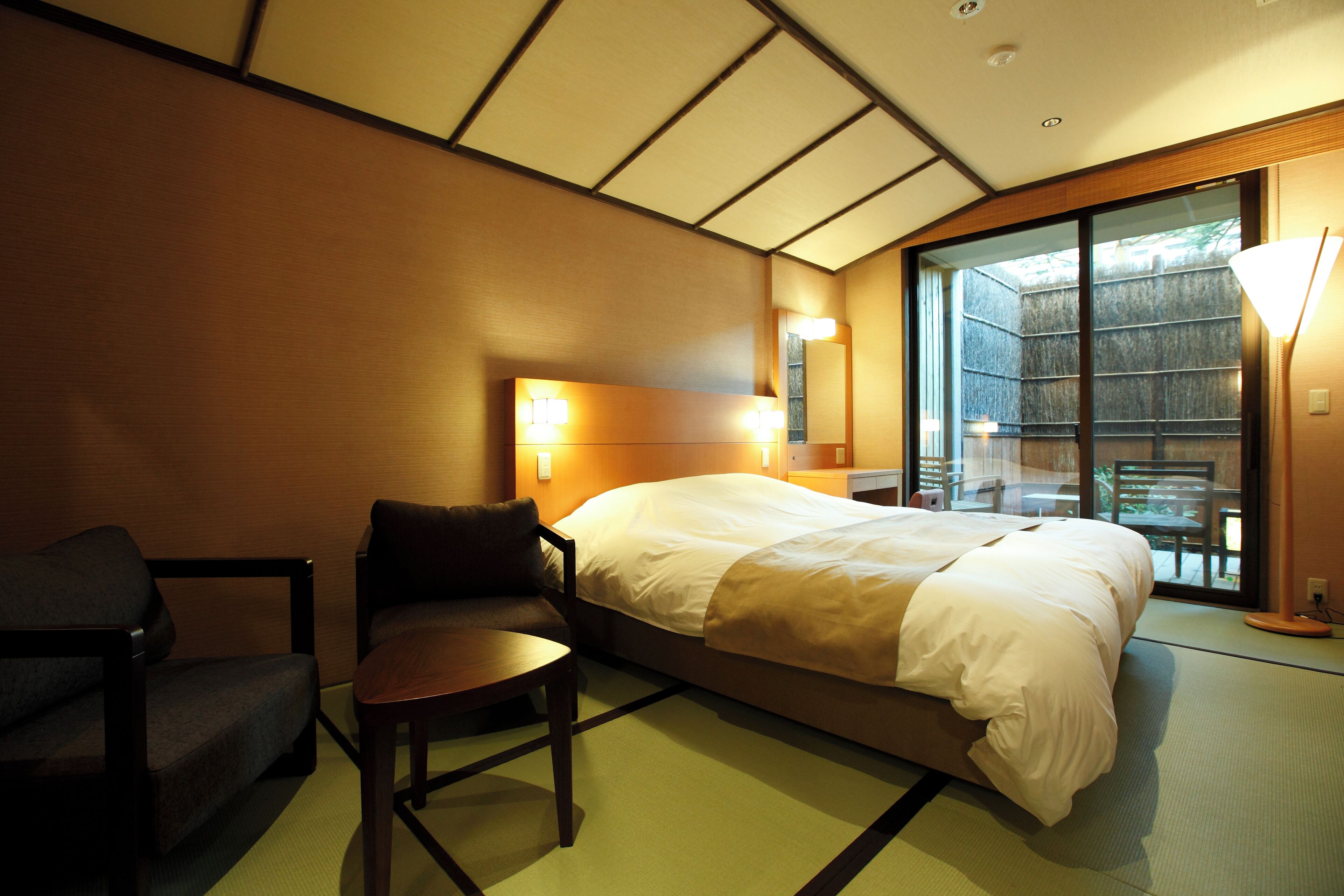 Quarto de hotel com uma cama, uma cadeira, uma mesa e uma janela grande com vista.