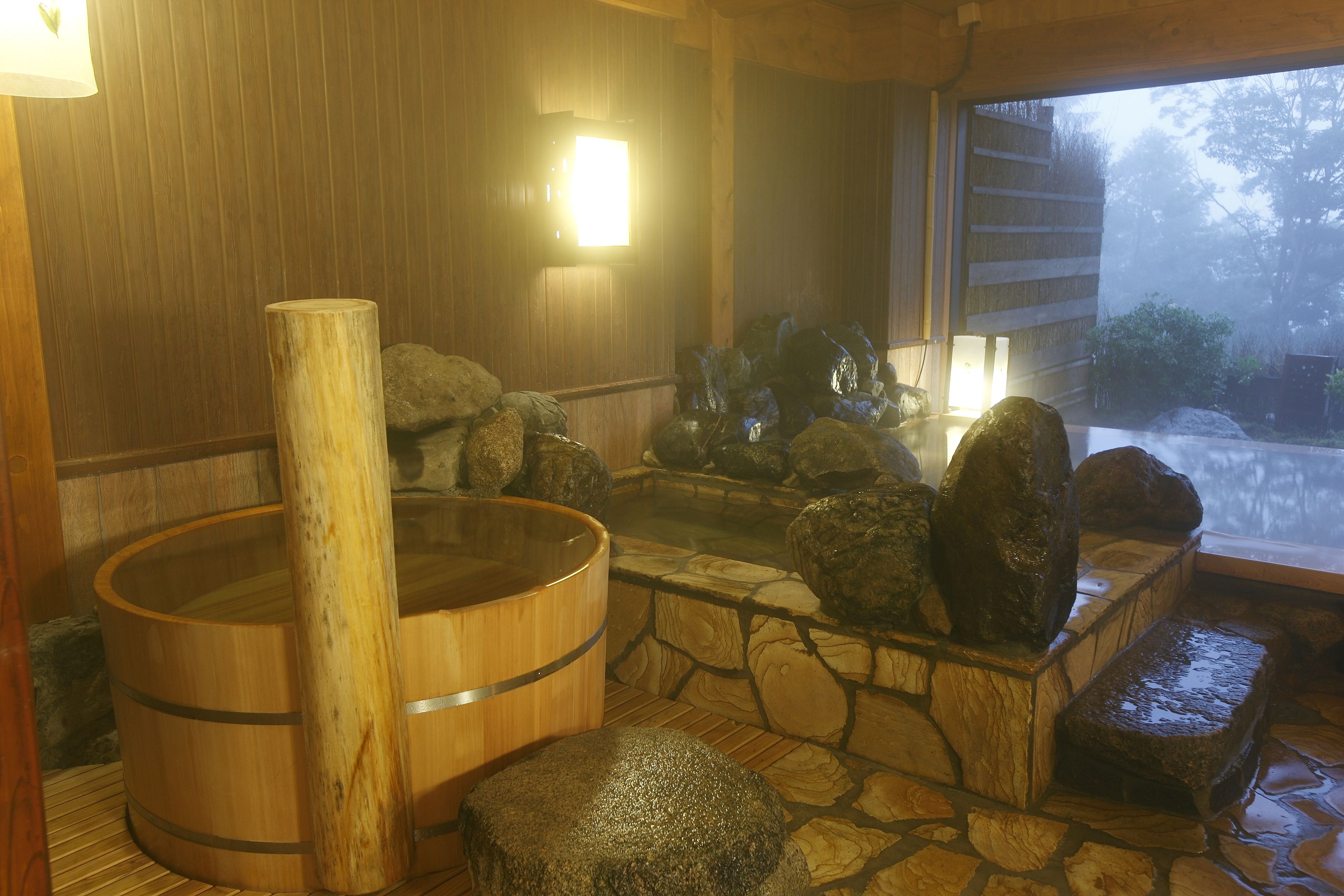 A traditional Japanese onsen with wooden tubs, stone steps, and a view of the surrounding nature.