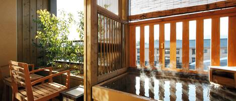 A traditional Japanese onsen with wooden flooring, a wooden bench, and a view of the sea through a bamboo screen.