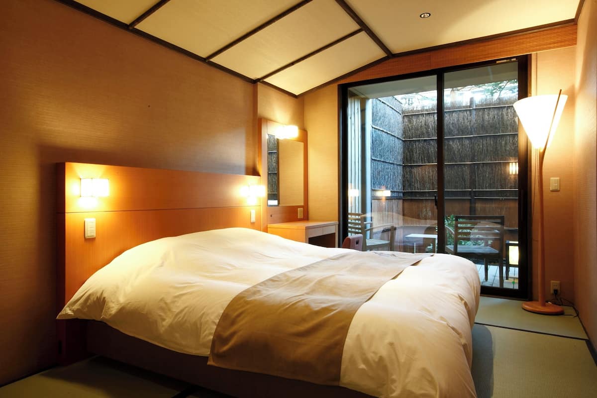 Une chambre d’hôtel avec un grand lit, un bureau, une chaise et une porte-fenêtre coulissante donnant sur un espace extérieur.