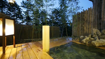 Una terraza de madera con fuente de agua cristalina, cerca de setos de bambú y un farol.