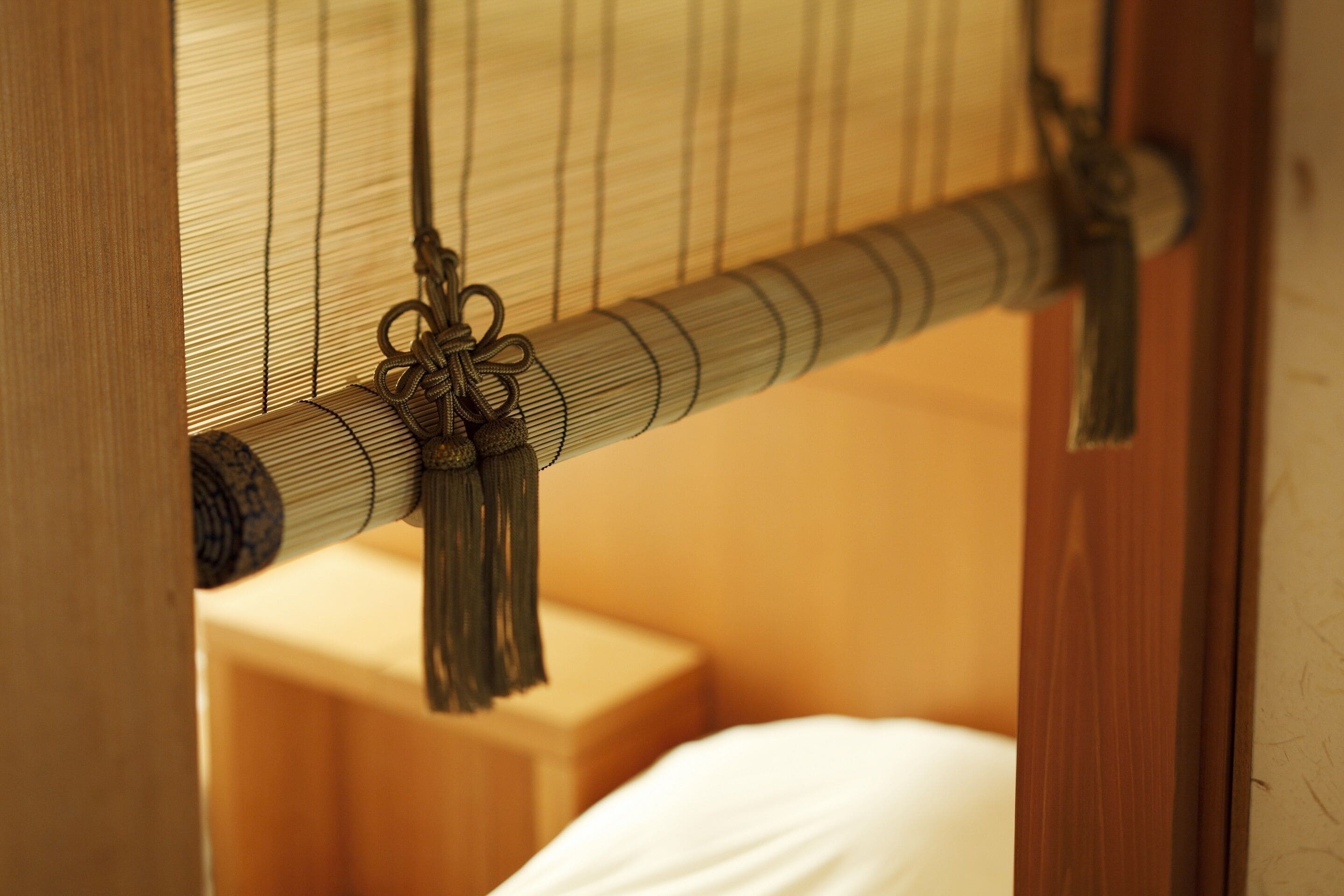 A close-up of a bed with a wooden headboard and a woven bamboo curtain.