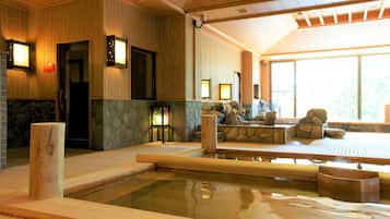 Un onsen japonés tradicional con un baño de piedra, bancos de madera y vistas al exterior a través de amplios ventanales.